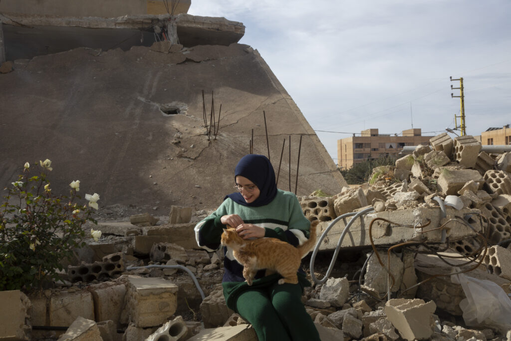 Batoul Hamza klappar en gatukatt bland ruinerna av en förstörd byggnad, intill RDFL-ActionAids kontor i staden Baalbek i Bekaadalen i östra Libanon, torsdagen den 12 december 2024.